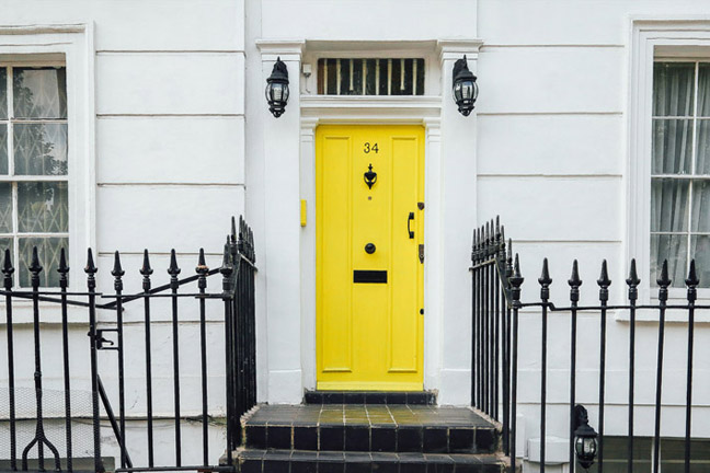Yellow front door behind black iron railings